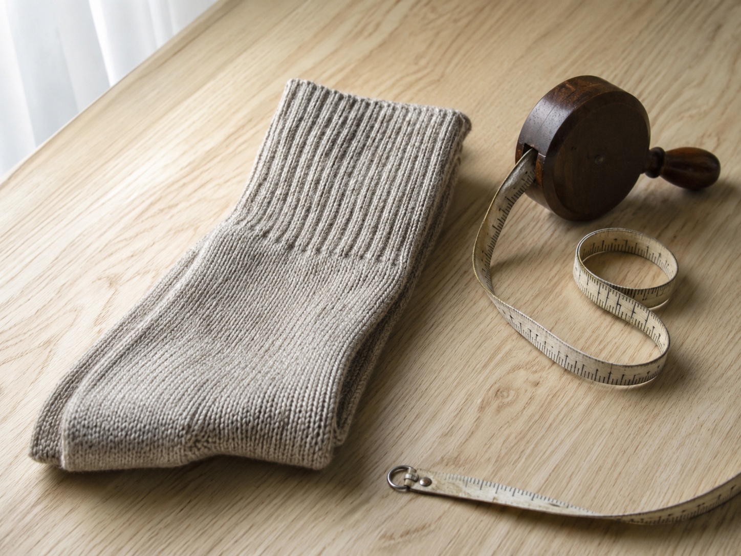 A folded ribbed knitted sock beside an uncoiled cloth tape measure