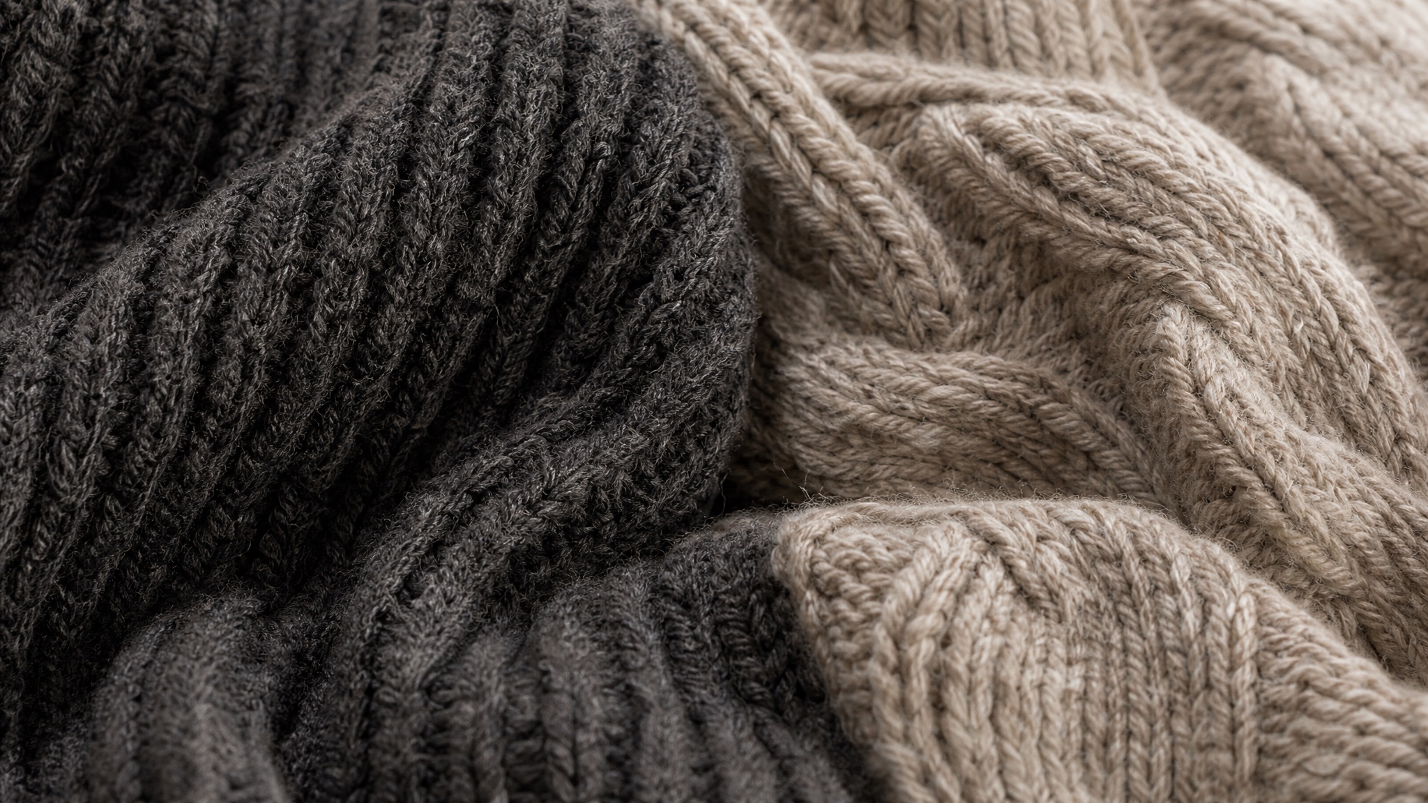 Close detail of overlapping charcoal ribbed and oatmeal cable knitted fabric